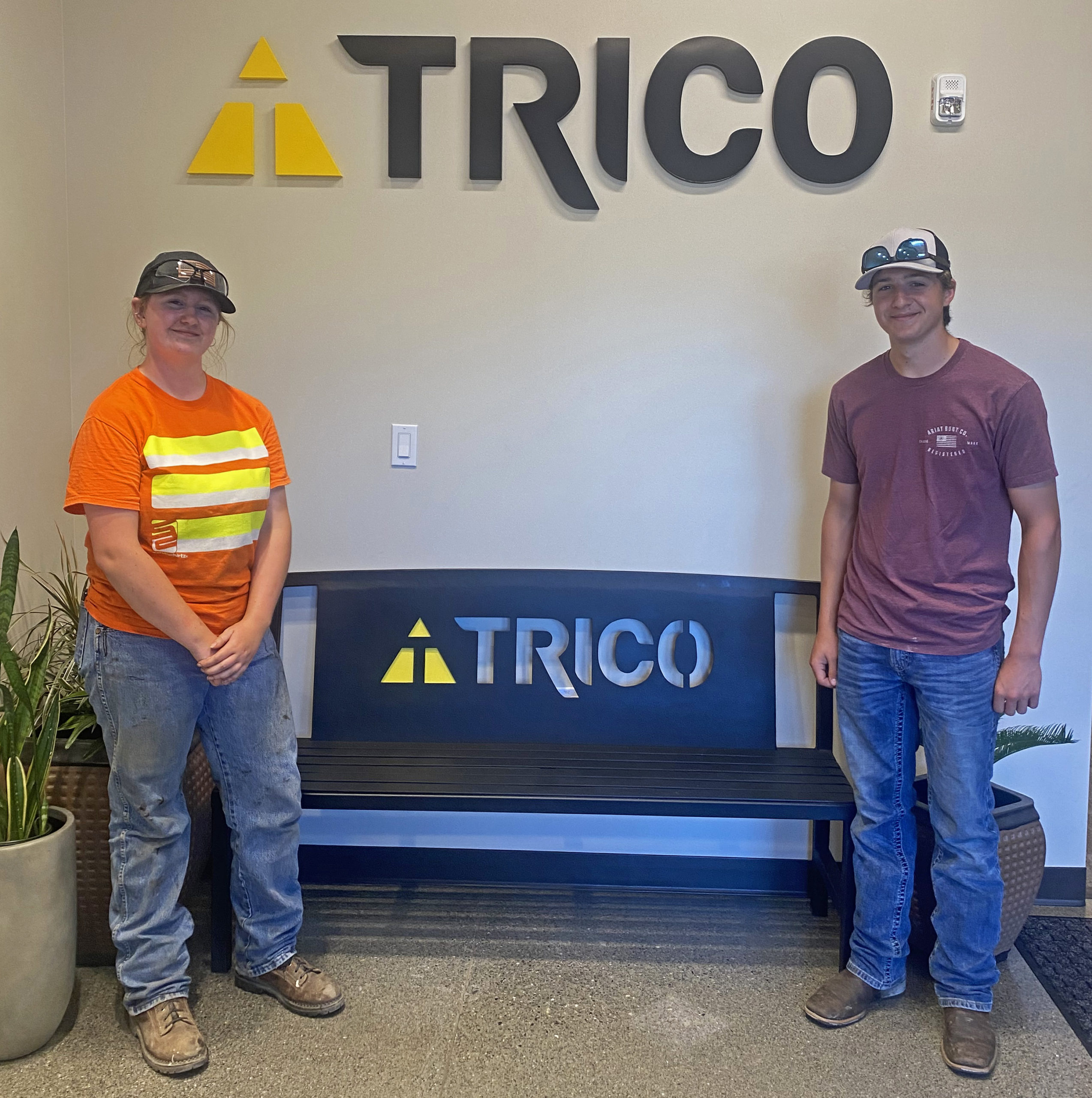 Two trico employees standing next to a trico bench